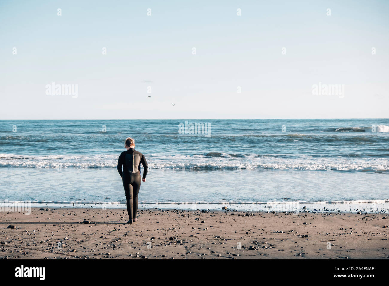Le Tween garçon porter une combinaison isothermique marcher dans les vagues à la plage Banque D'Images