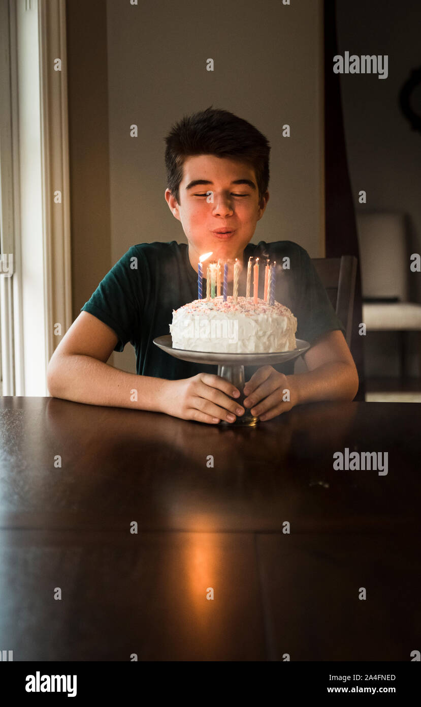 Teen boy blowing out les bougies sur son gâteau d'anniversaire à la table. Banque D'Images