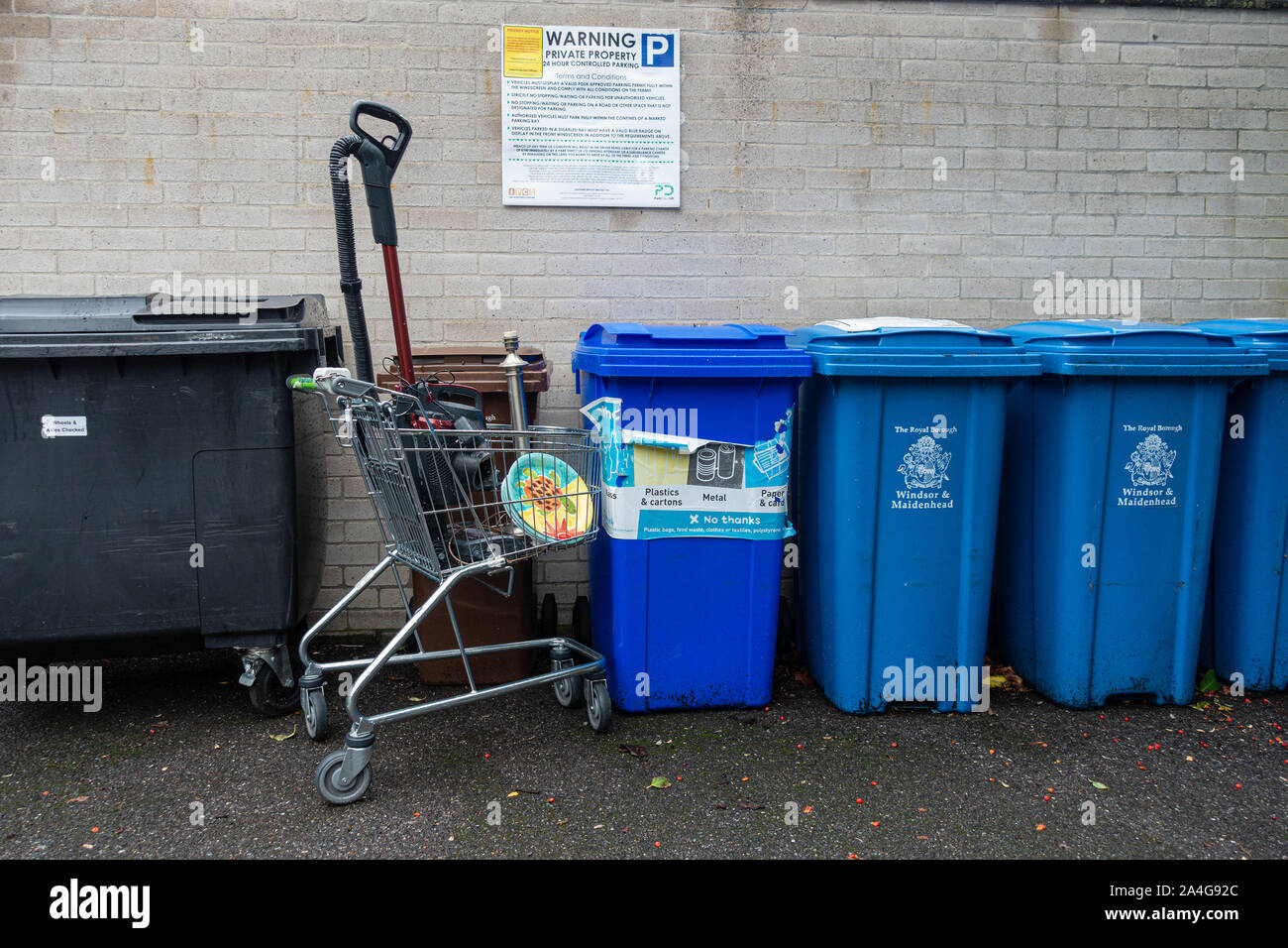 Wheelie bins et un chariot de supermarché contenant des détritus abandonnés à côté d'un mur de briques avec un signe sur des interdictions de stationnement. Banque D'Images