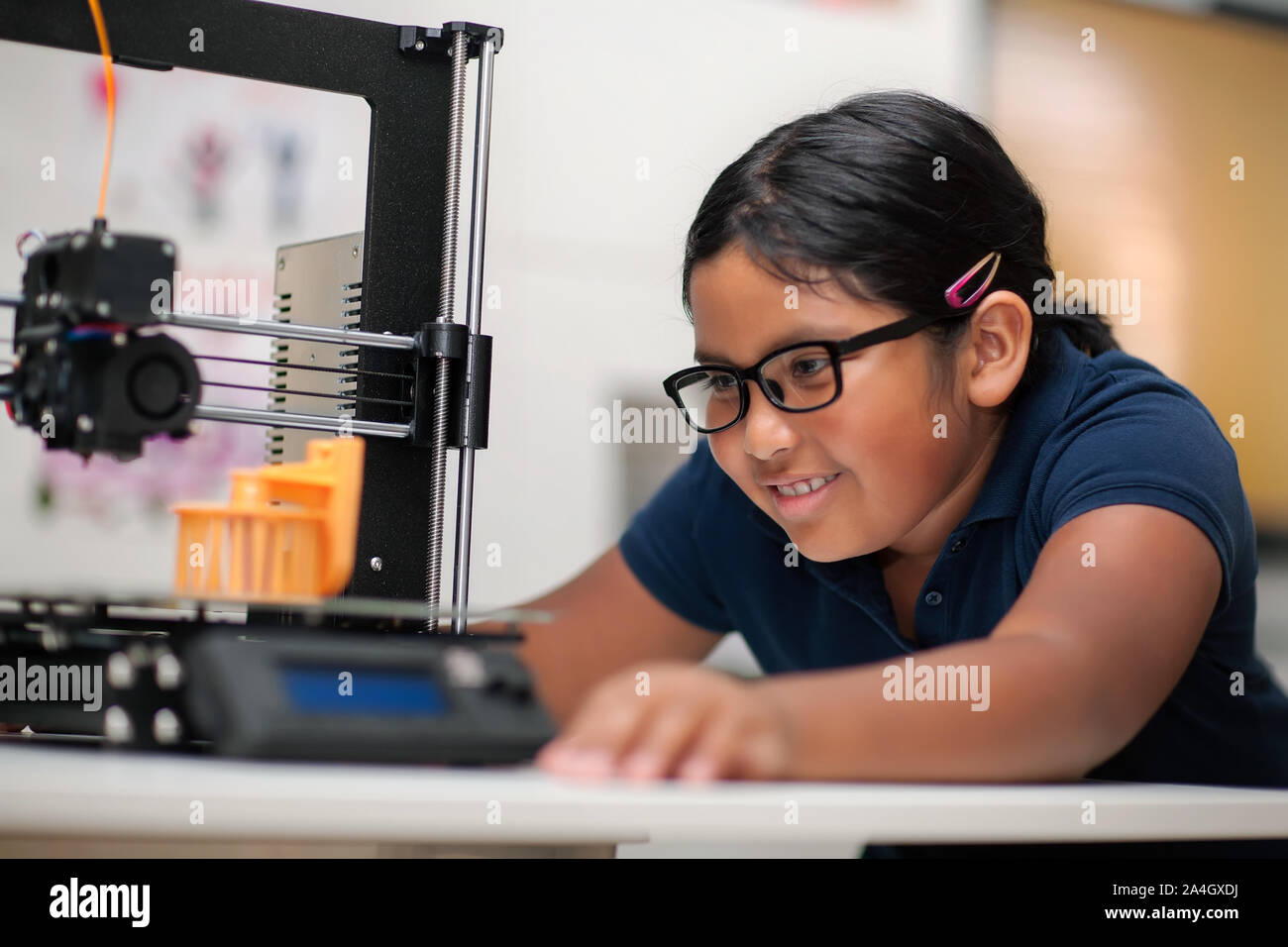 Un heureux jeune fille portant des lunettes et regarder une imprimante 3d terminer le modèle 3D qu'elle a créé. Banque D'Images