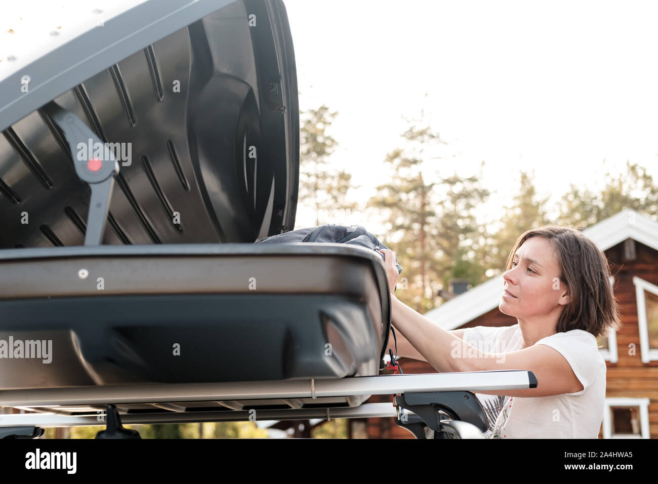 Satisfait femme met les choses dans le toit de la voiture ou dans la boîte de chargement, avant un voyage en famille en vacances. Close-up. Banque D'Images