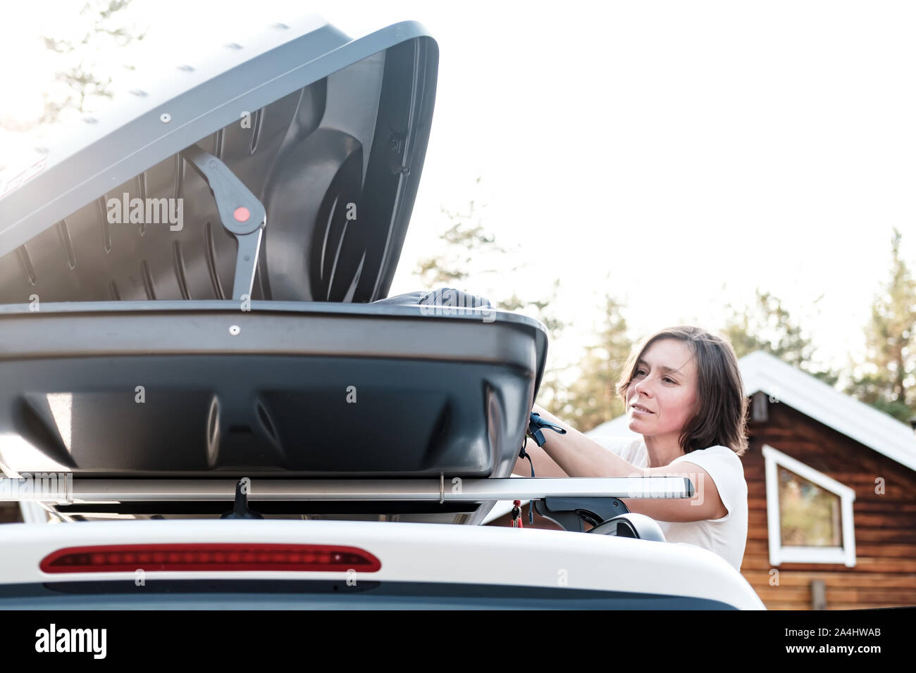 Satisfait femme met les choses dans le toit de la voiture ou dans la boîte de chargement, avant un voyage en famille en vacances. Close-up. Banque D'Images