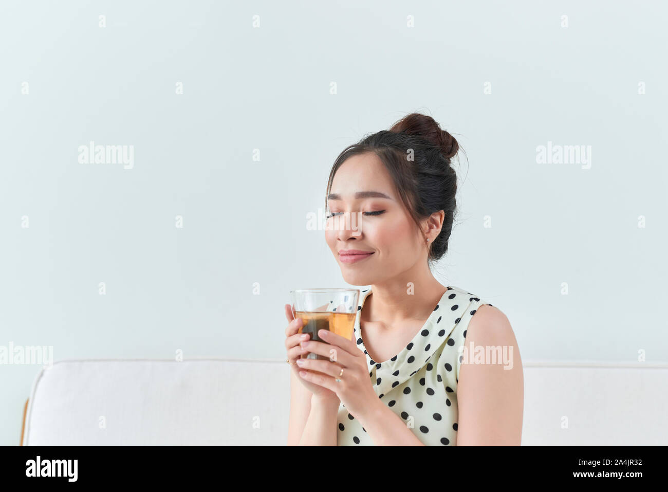 Happy asian woman sitting on sofa holding sa tasse à la maison Banque D'Images