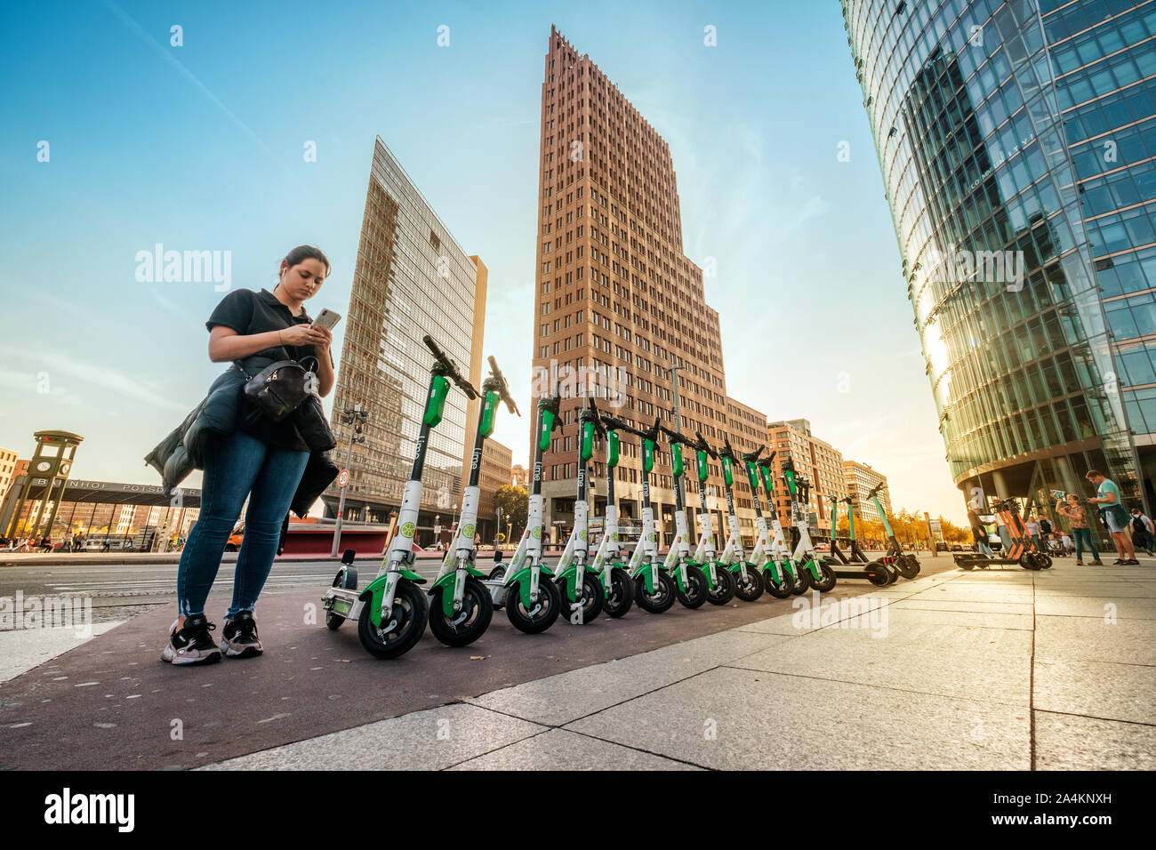 Berlin, Allemagne - Octobre 2019 : Girl on mobile phone app maintenant de scooters électriques E , escooter ou e-scooter de la société LIME sur trottoir à Berlin Banque D'Images