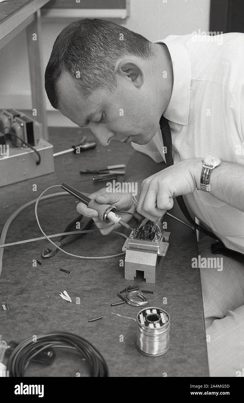 Années 1960, historique, un étudiant adulte travaillant dans un atelier, utilisant un fer à souder sur une boîte à fusibles électrique, USA. Banque D'Images