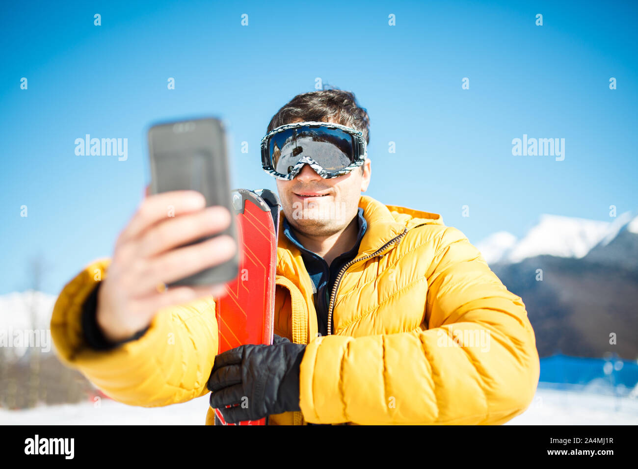 Photo de smiling man in ski mask à prendre des photos de lui-même dans l'après-midi contre le ciel bleu et arbres Banque D'Images