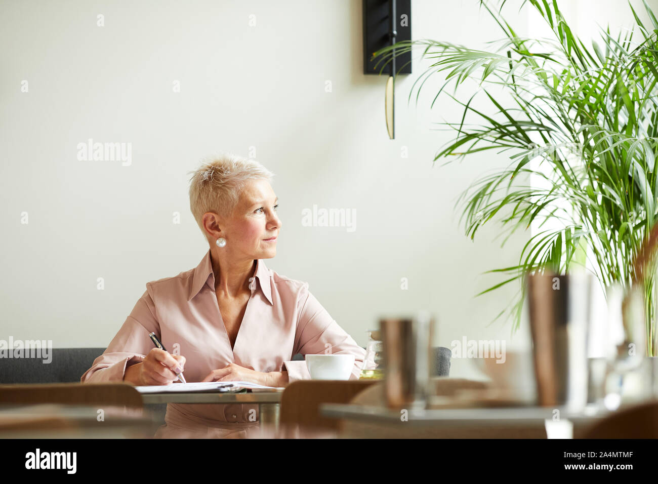 Femme mature avec de courts cheveux blonds à l'écart tout en travaillant à la table at office Banque D'Images