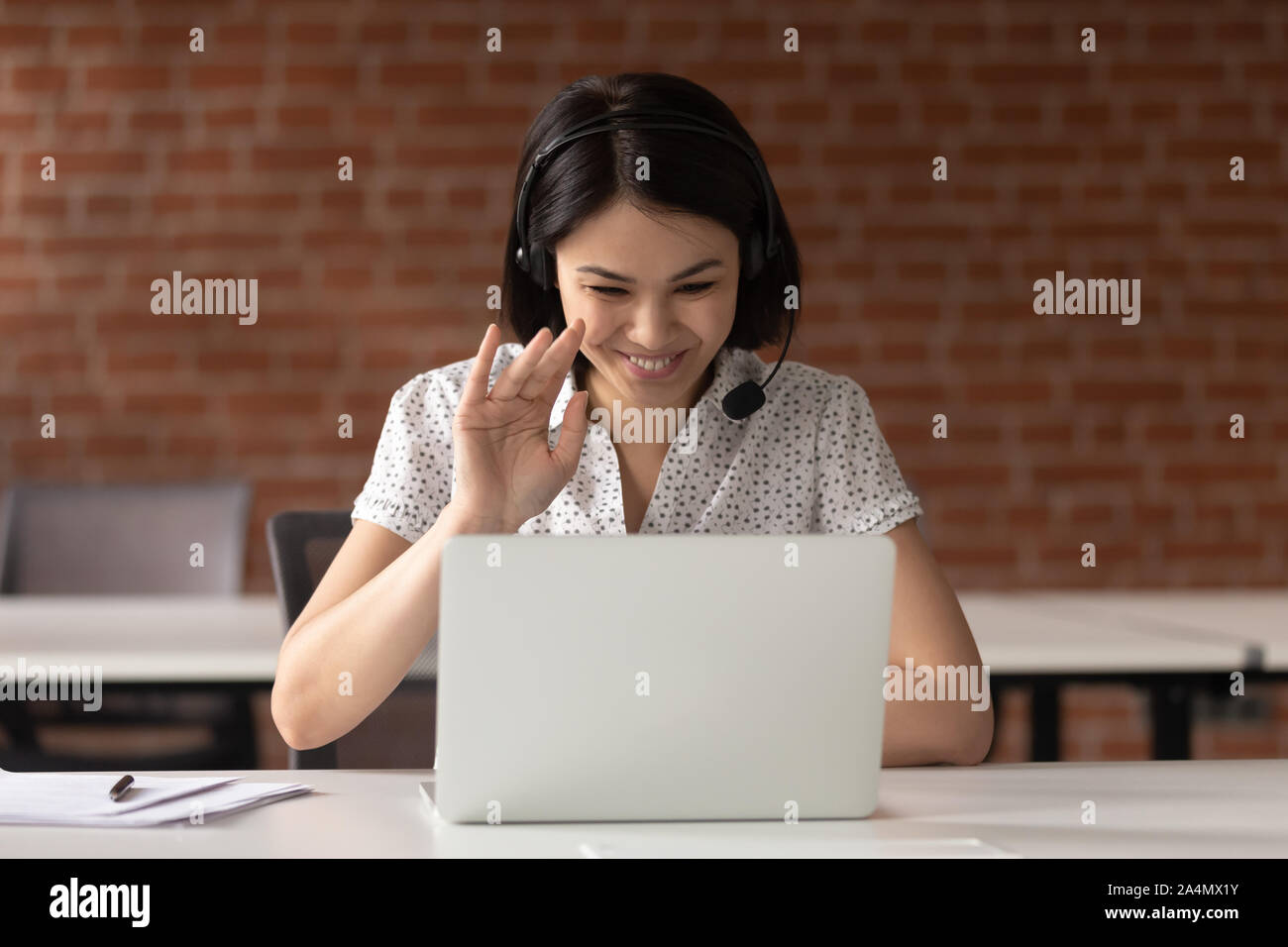 Smiling Asian businesswoman casque en agitant la main, using laptop Banque D'Images