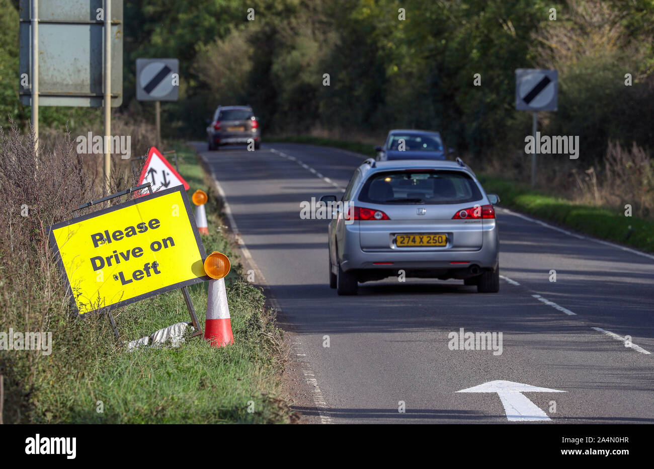 Un véhicule avec des plaques diplomatiques transmet une Veuillez conduire sur la gauche signe et signalisation qui ont été placées sur la B4031 en dehors de RAF Croughton, dans le Northamptonshire, où Harry Dunn, 19 ans, est mort lorsque sa moto a été impliqué dans une collision frontale en août. Banque D'Images