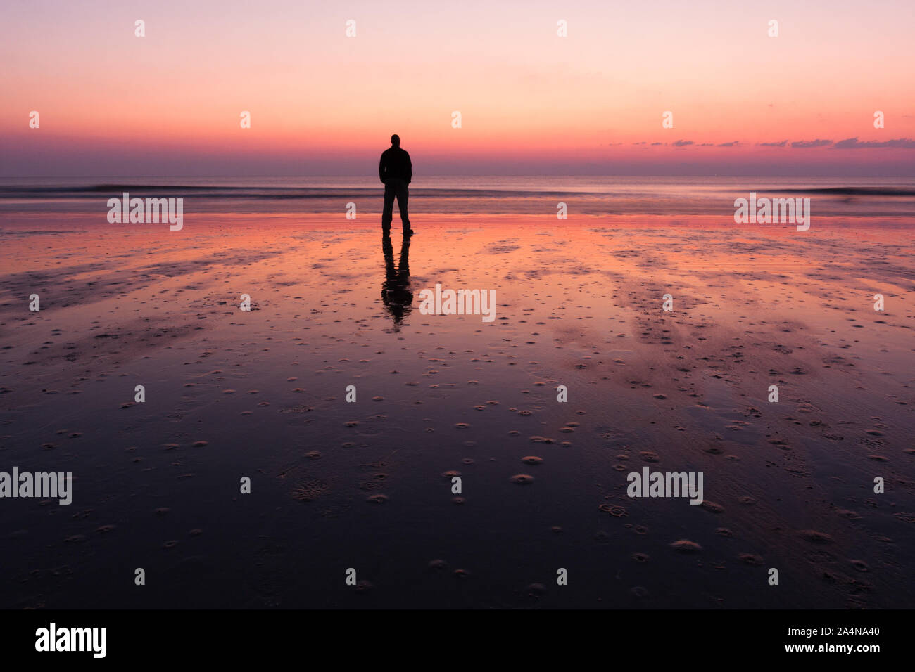 La silhouette d'un homme seul dans la solitude à l'aube sur la plage. Banque D'Images