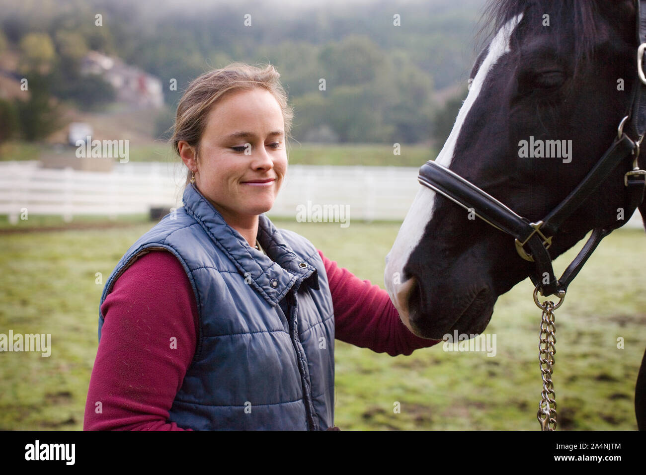 Jeune femme debout dans un enclos avec son cheval. Banque D'Images