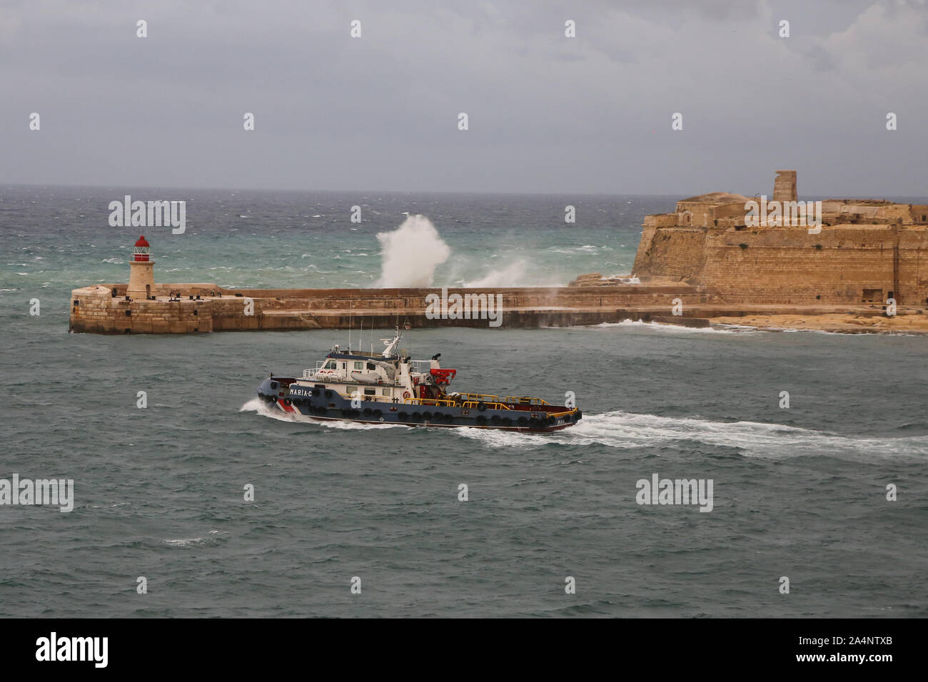 Les vagues déferlent sur Ricasoli brise-lames est comme le bateau remorqueur Maria C quitte le Grand port sur l'île de Malte Banque D'Images