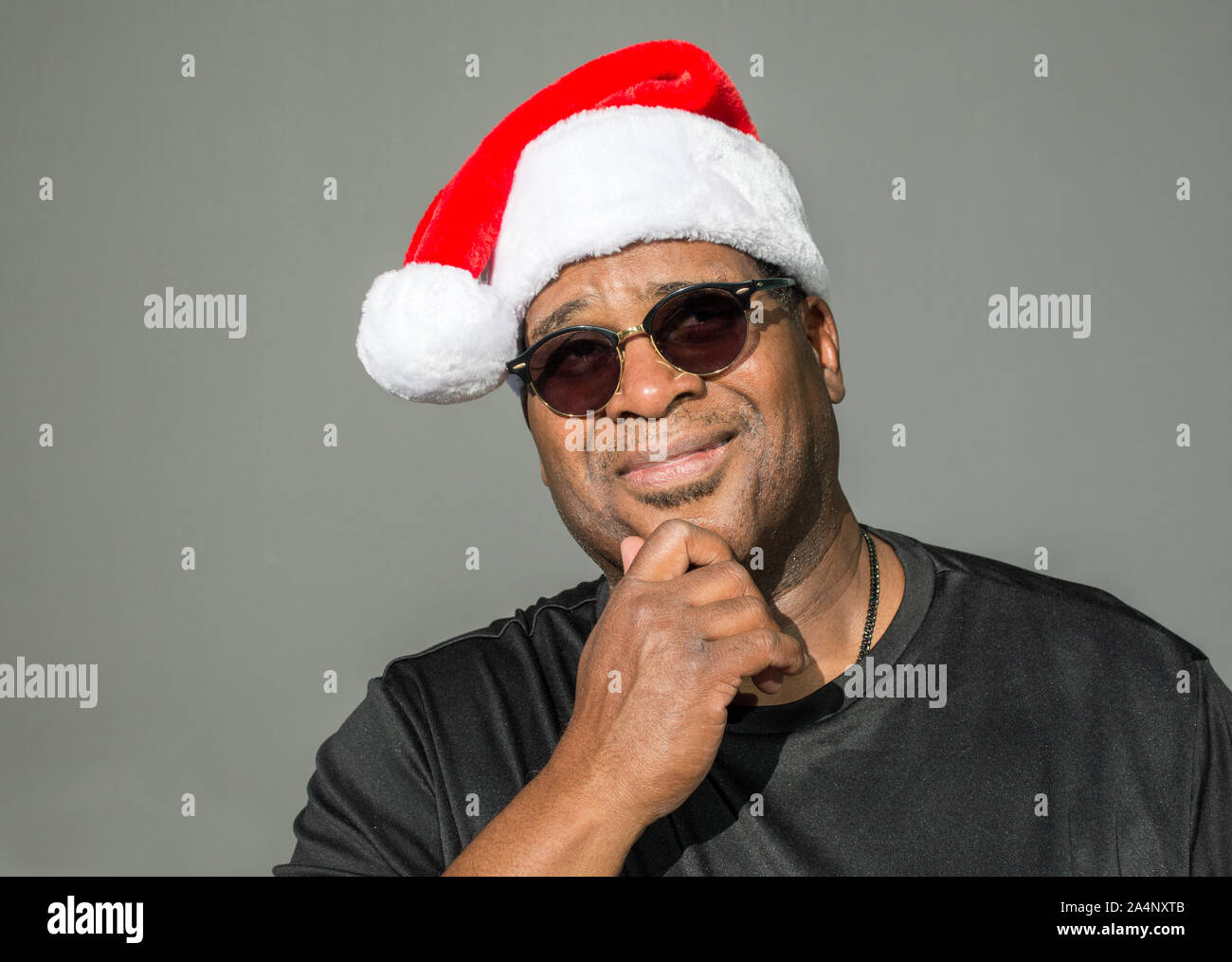 Smiling African American man avec sa main sur son menton, le port d'un Père Noël rouge et blanc sur un fond uni hat Banque D'Images