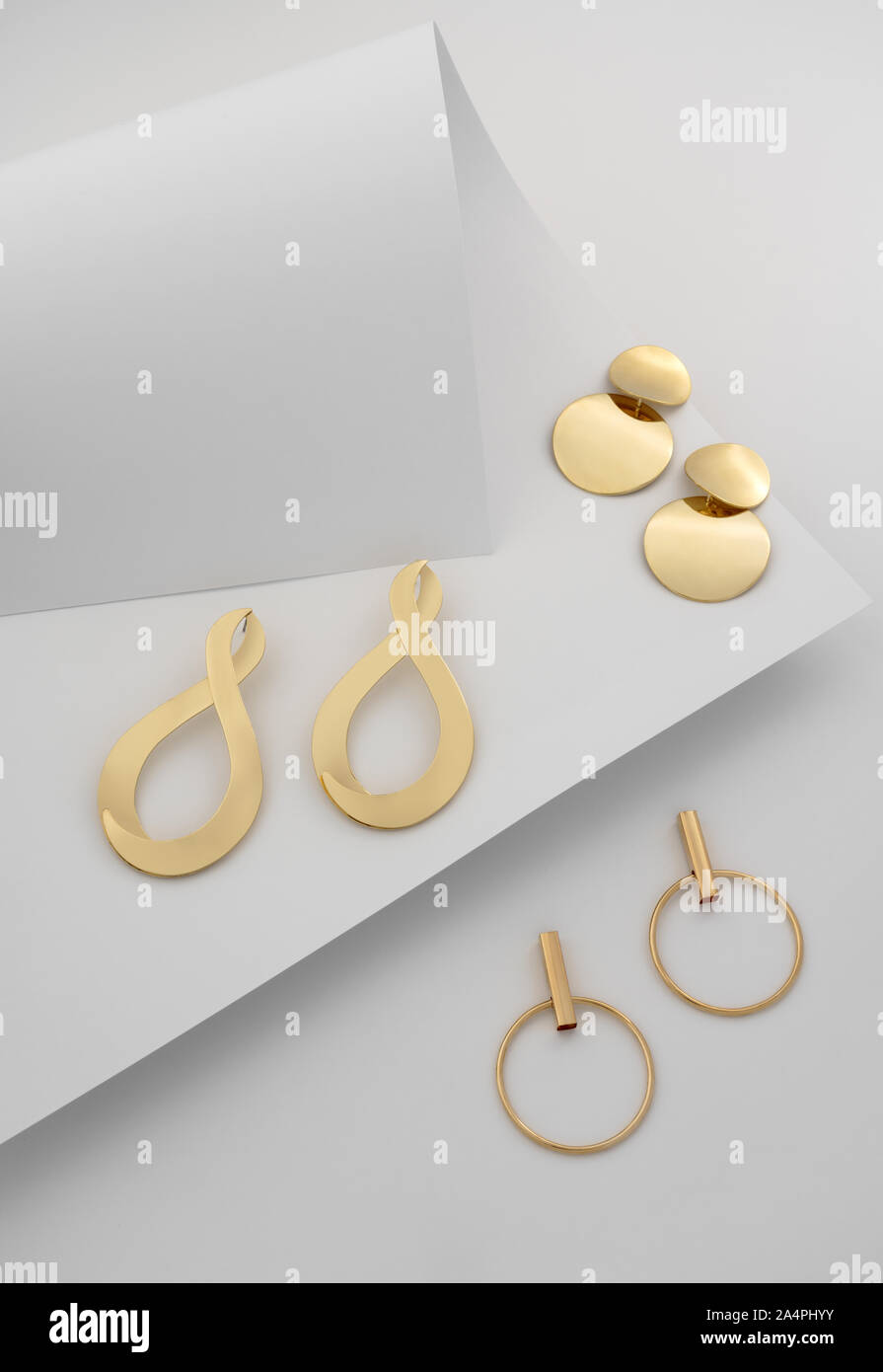 Vue supérieure, trois paires de boucles d'or sur fond de papier blanc plié Banque D'Images