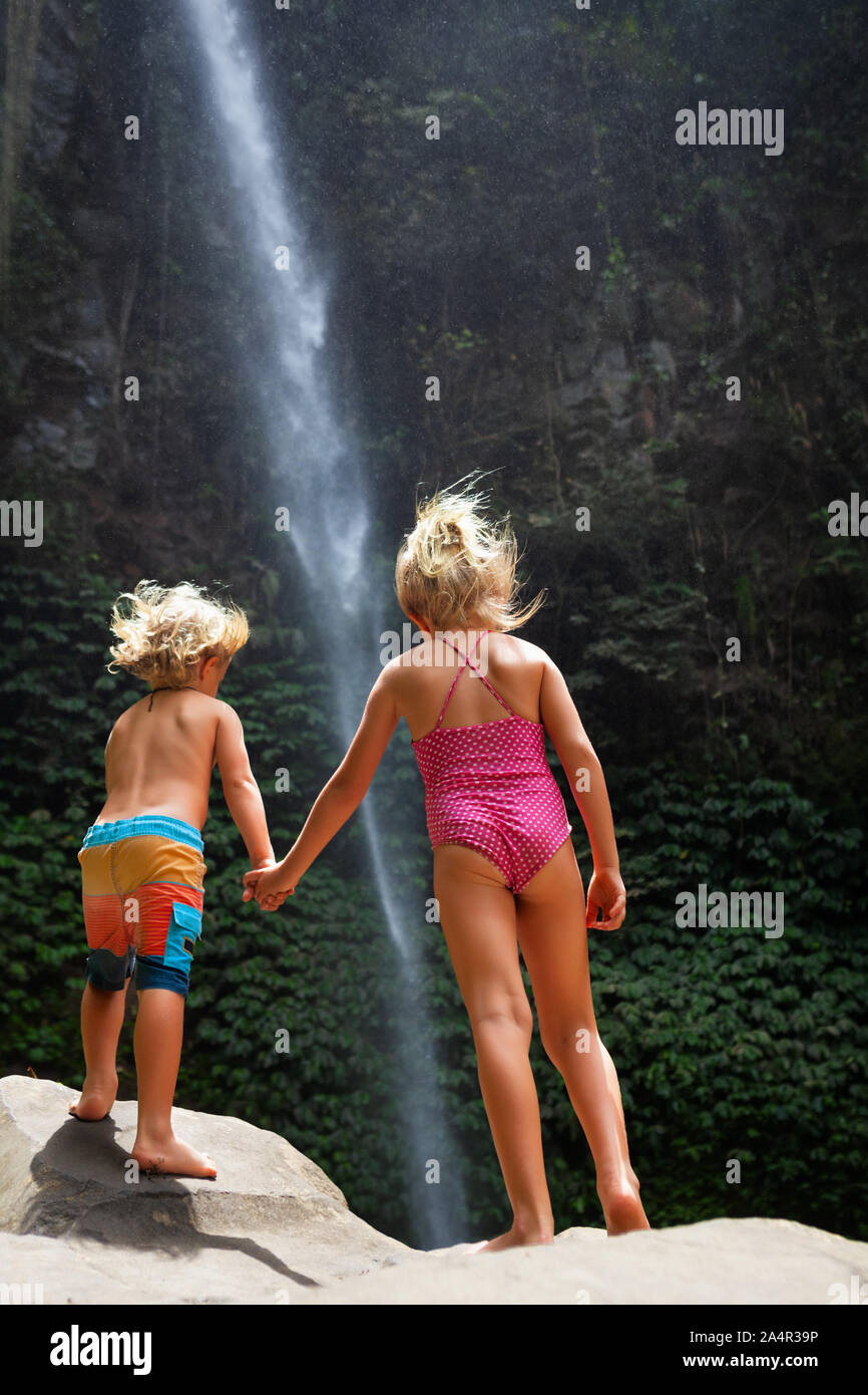 Dans la jungle tropicale heureux sœur se tenir sous une cascade, explorer la nature de la forêt tropicale. Voyage d'aventure pour les enfants, randonnée vie activité avec enfant. Banque D'Images