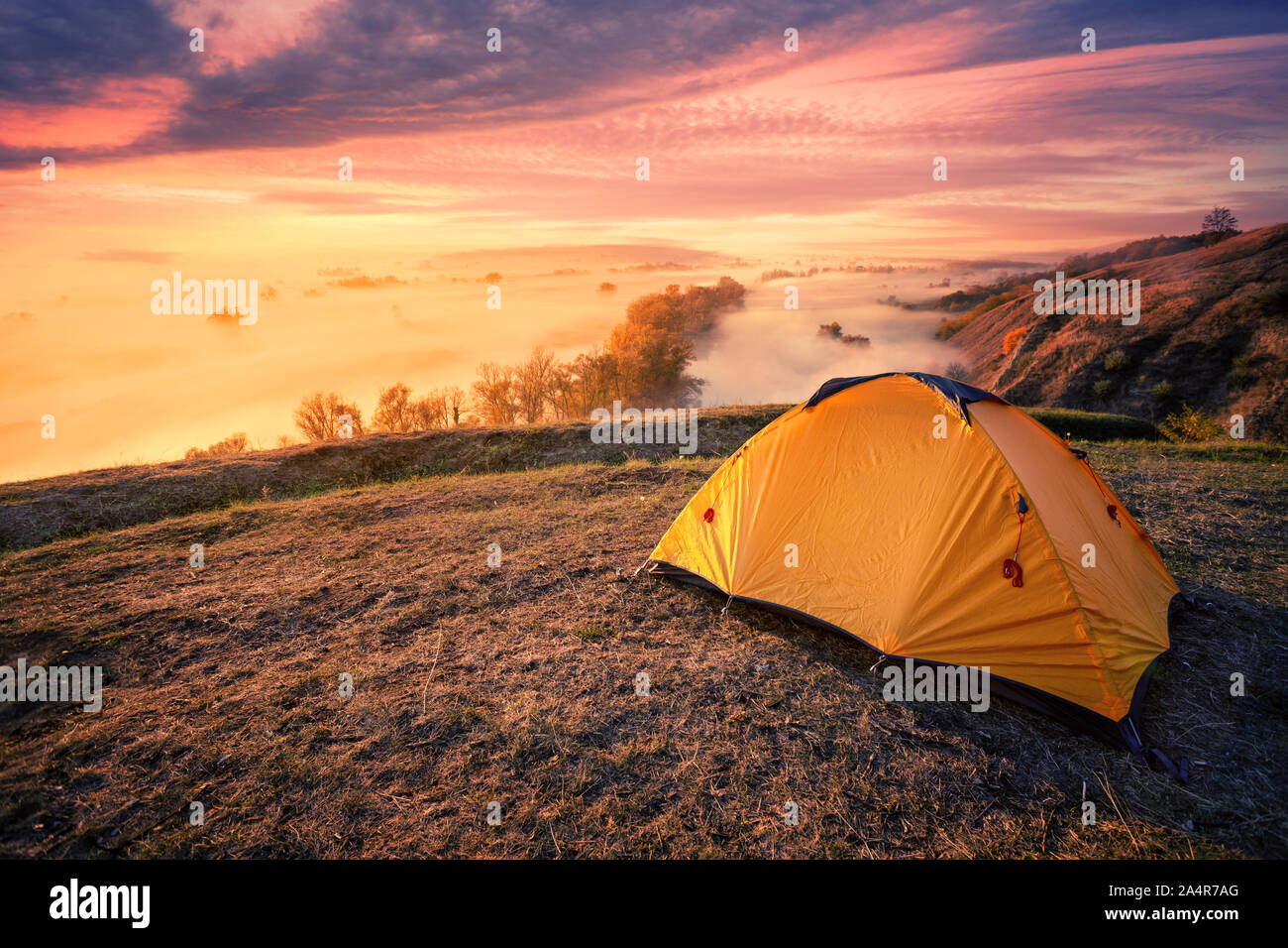 Tourisme Orange tente sur une colline au-dessus d'une rivière de brouillard. Ciel coucher de soleil spectaculaire. Billet et privacy concept Banque D'Images
