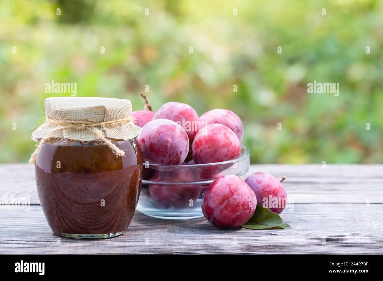 Les prunes dans un bol transparent et pot de confiture de prunes sur la table en bois. Fond vert naturel Banque D'Images