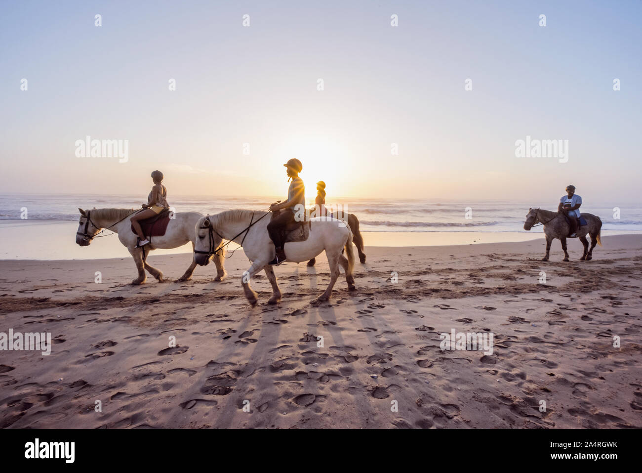 Les gens de l'équitation au coucher du soleil sur la plage Banque D'Images
