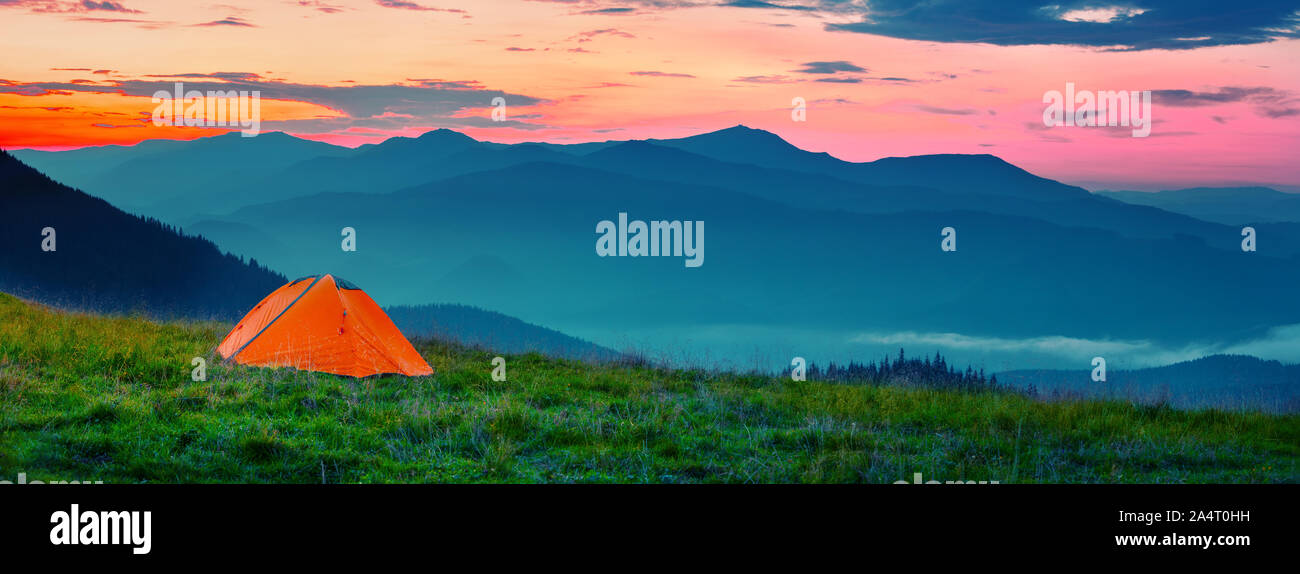 Orange tente dans la montagne au coucher du soleil Banque D'Images