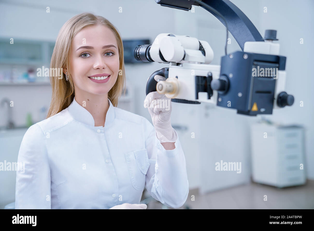 Adorable blonde femme travaillant comme stomatologist dans secteur de la dentisterie clinique. Cheerful dentiste looking at camera, souriant et posant. Spécialiste travaillant avec du matériel moderne comme microscope. Banque D'Images