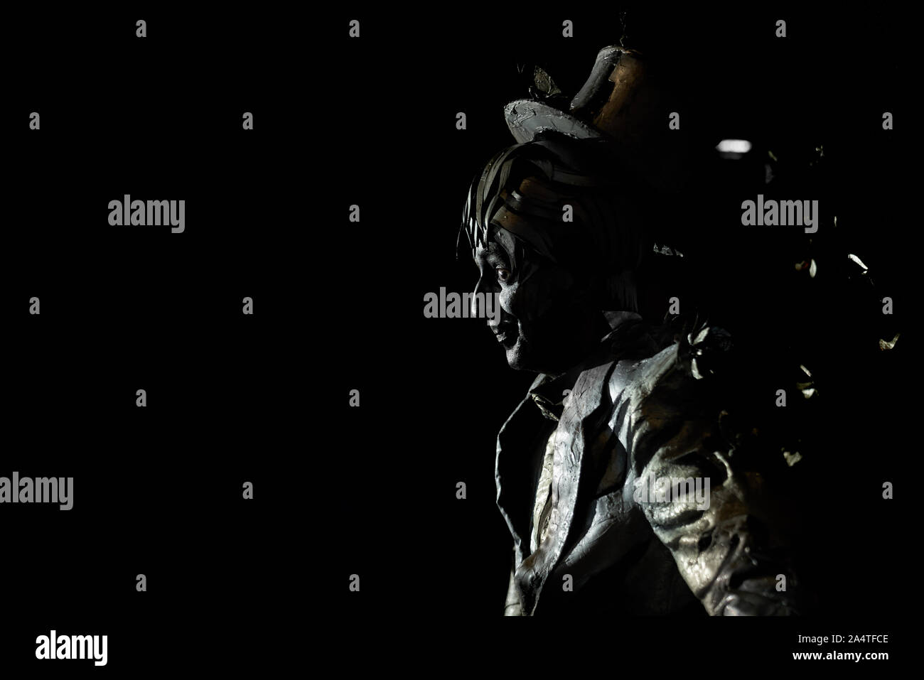 Vue latérale du mime énigmatique habillés en costume d'or noir étrange et portant haut de forme sur sa tête.L'acteur talentueux imitant une statue ou caractère de conte de fées sur fond noir Banque D'Images