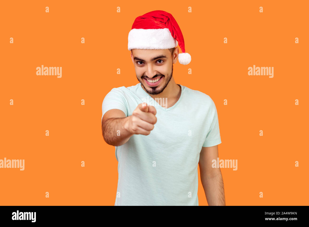 Hey you ! Portrait de jeune homme barbu joyeux in santa hat et occasionnels t-shirt blanc, debout face à la caméra et à pleines dents avec sourire. Banque D'Images