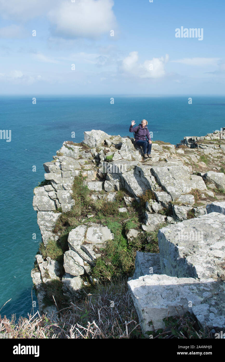 Femme assise sur un haut walker barre rocheuse au-dessus de la mer dans la Vallée des Roches, Lynton, Devon. Banque D'Images