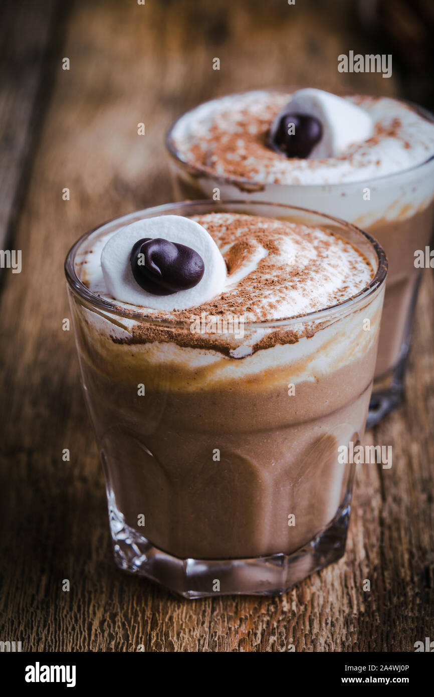 Happy monster, pumpkin spice latte de crème fouettée et de grands yeux de guimauve sur le dessus, dans des verres à dessert d'Halloween Banque D'Images