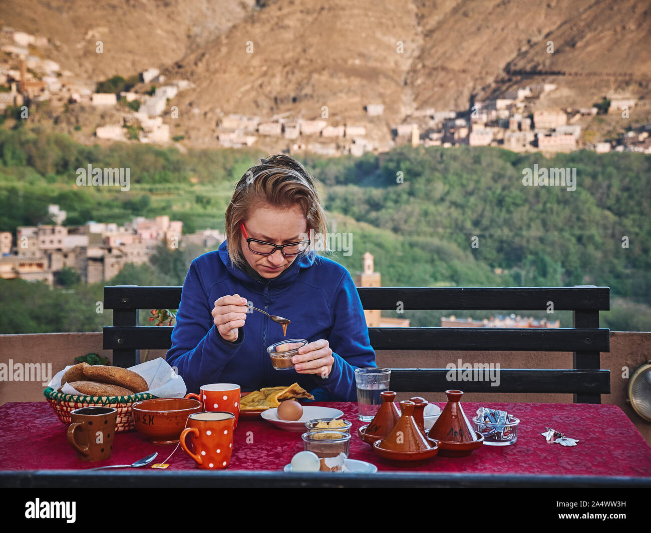 Caucasian blonde hlaving avec petit-déjeuner typiquement marocain citoyennes Comment devenir coopérant Volens et crêpes sur la terrasse avec belle vue à Imlil Maroc Haut Atlas Banque D'Images