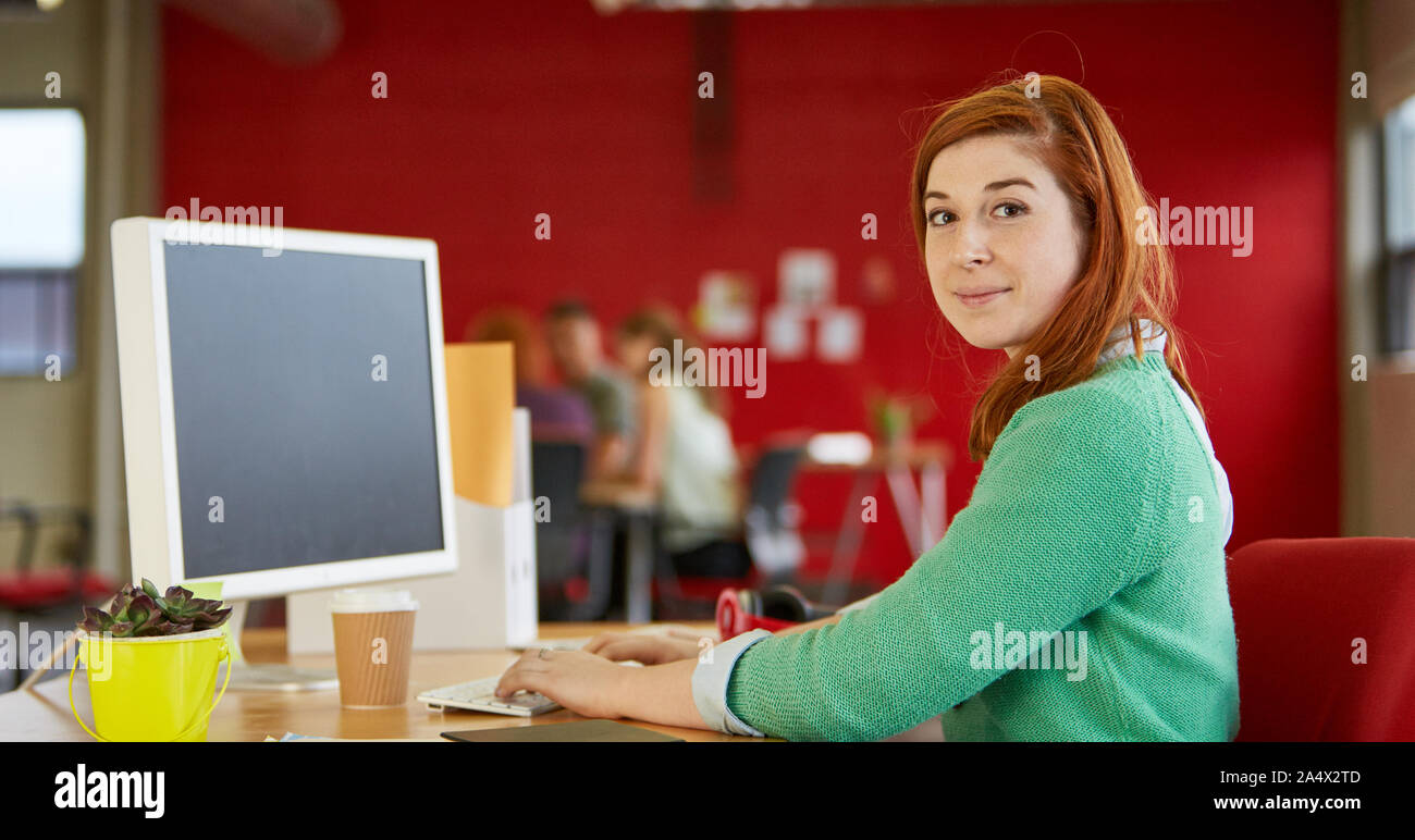 Confident female designer travaillant à son bureau en rouge de créatif Banque D'Images