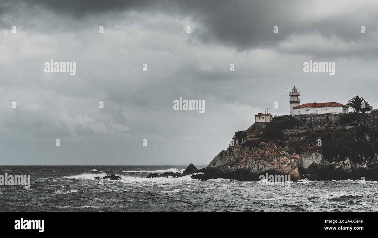 Vue panoramique du phare sur falaise sur un jour de tempête avec mer agitée et le ciel gris avec des nuages, Cudillero, Asturias, Espagne. Banque D'Images