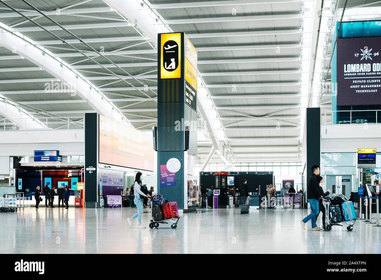 Les passagers à pied à l'intérieur de l'aéroport international de Londres Heathrow Terminal 5 hall des départs. Femme Asiatique porte un masque et pousse avec une assurance dans le panier. Banque D'Images