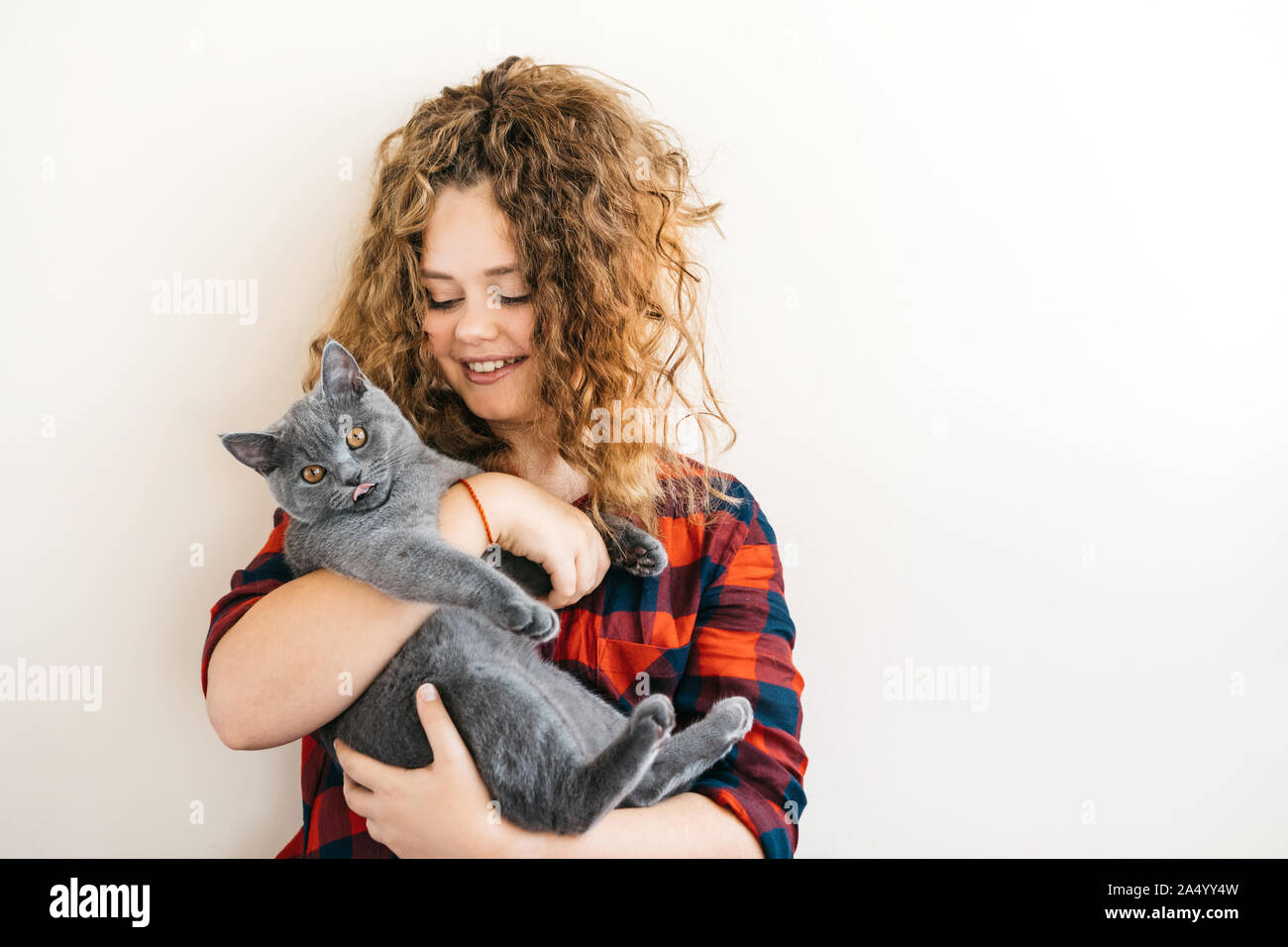 Curly blonde woman smiles et tient dans sa main un chaton gris Banque D'Images