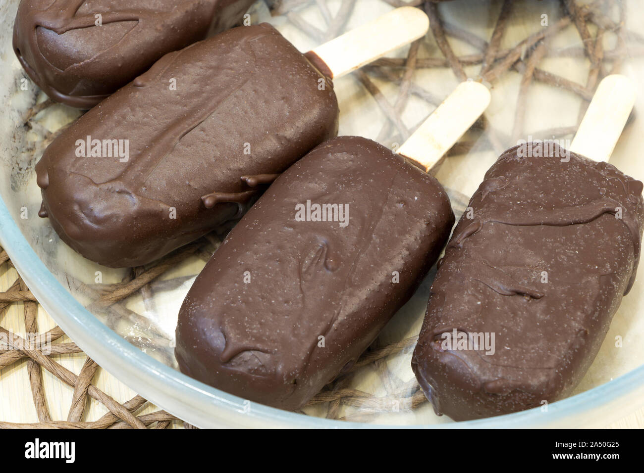 Matières premières fraîches les sucettes glacées sur bois enduit de lustre de chocolat réside dans le bol transparent verre nappe en osier. Vegan délicieux dessert maison. Haut Banque D'Images