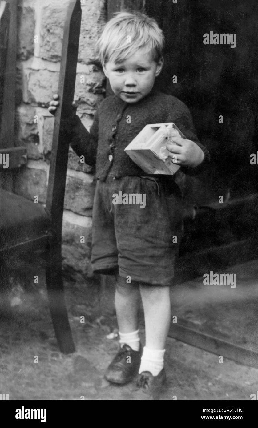 Petit garçon de 4 ans une famille ouvrière vêtus de shorts et de cardigan debout dans l'embrasure d'une holding toy en fer-blanc. Angleterre 1956 Banque D'Images
