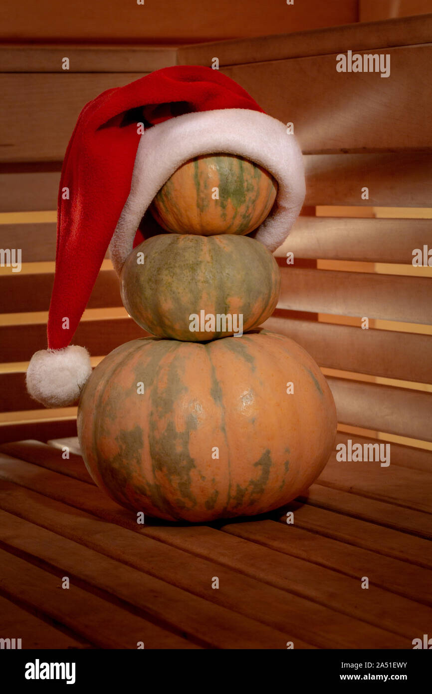 Une pyramide de trois citrouilles sur une surface en bois est orné d'un chapeau de Père Noël. À travers les murs en lattes de bois lumière transperce avec beaut Banque D'Images