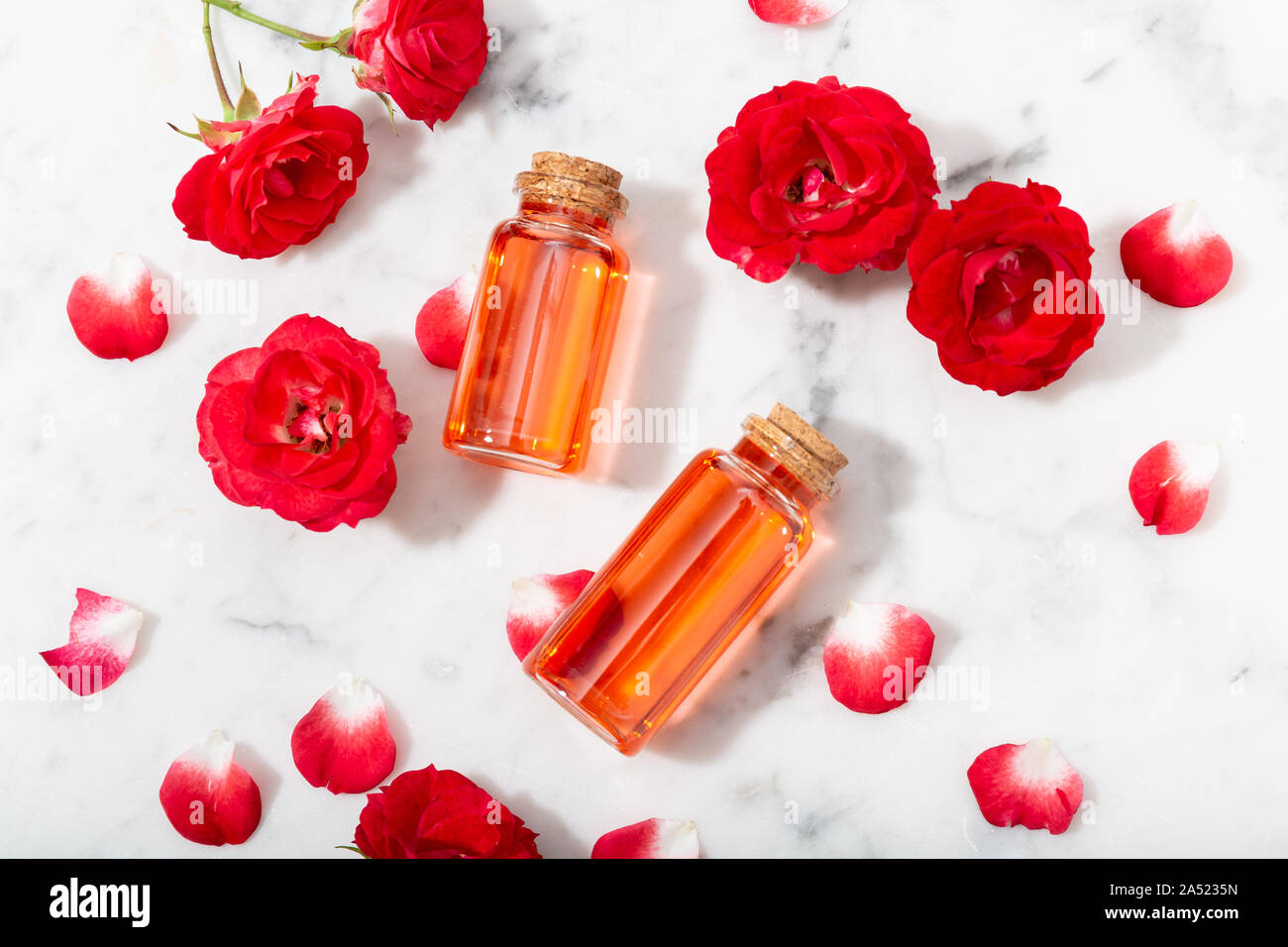 L'eau de rose parfumée dans le flacon en verre et de petites roses rouges de pétales . Massage, aromathérapie et cosmétiques bio concept Banque D'Images