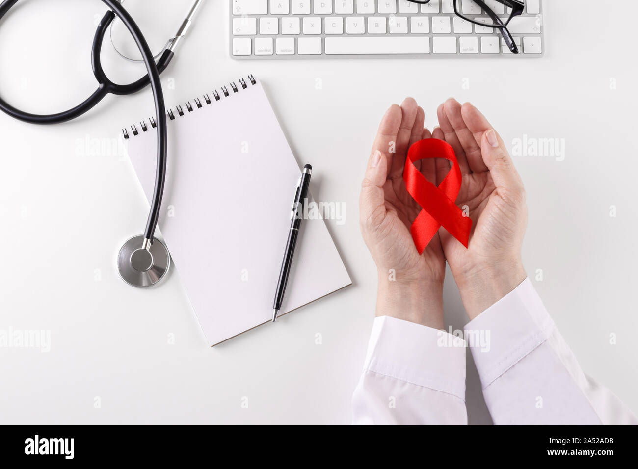 Doctor holding ruban rouge dans les mains la journée mondiale contre le cancer concept ,coin au bureau avec clavier lunettes stethoscope Banque D'Images