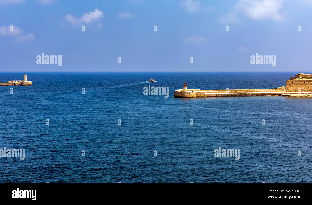 Bateau dans la mer turquoise de l'eau entre La Valette avec brise-lames et phare lumière Breakwater Ricasoli à Grand Harbour East brise-lames. Banque D'Images