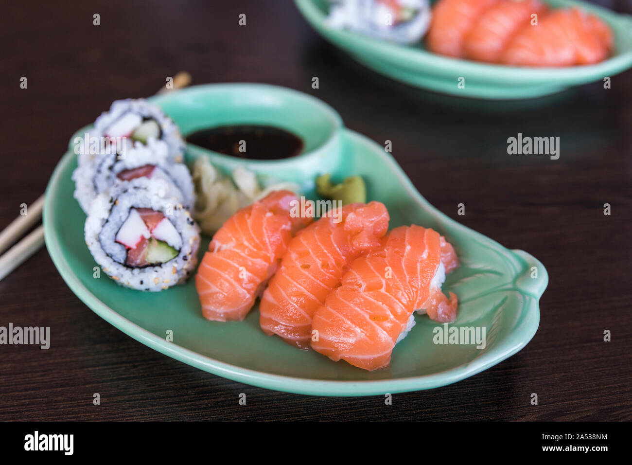 Une petite plaque sushi et Maki Nigiri avec sushi. Il y a des baguettes en bois à côté de la plaque qui se trouve sur une table en bois sombre. Banque D'Images
