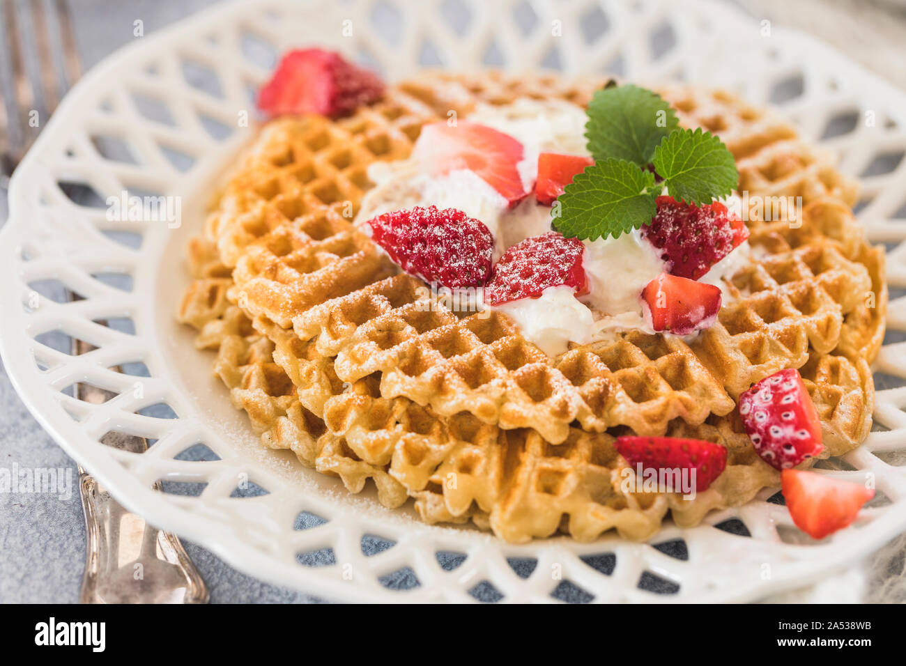Gaufres d'or frais avec des morceaux de fraises et crème fouettée sur le dessus. Plaque à motifs blancs sur fond gris. Banque D'Images