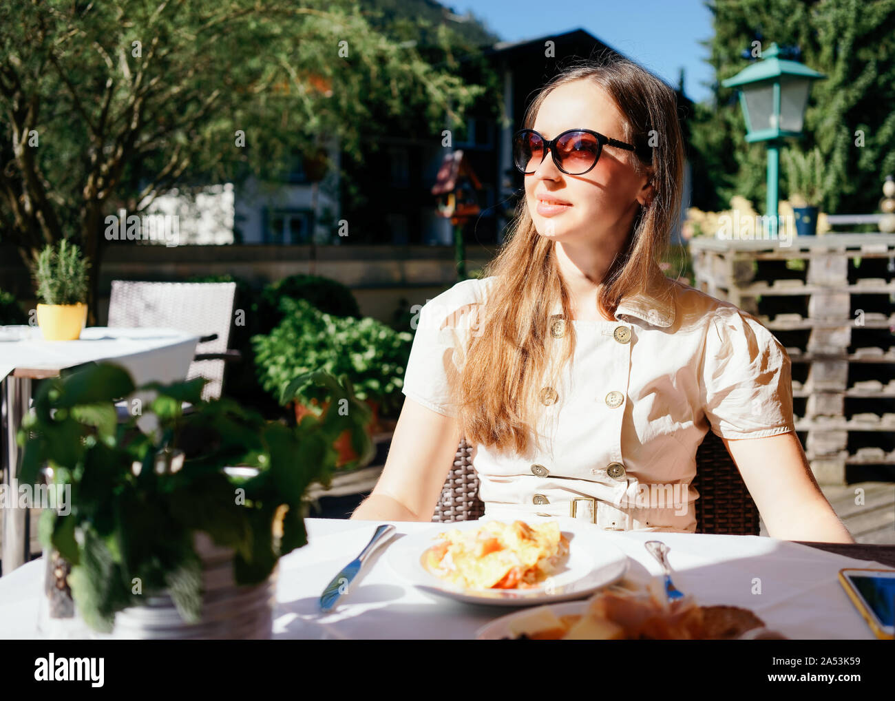 Jeune femme en robe et lunettes assis et prendre le petit-déjeuner Banque D'Images