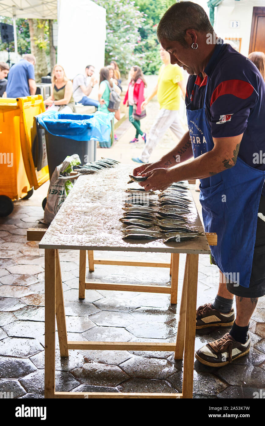 Homme salant des sardines embrochées sur une table lors d'un festival local dans le vieux port d'Algorta, Getxo, Espagne Banque D'Images