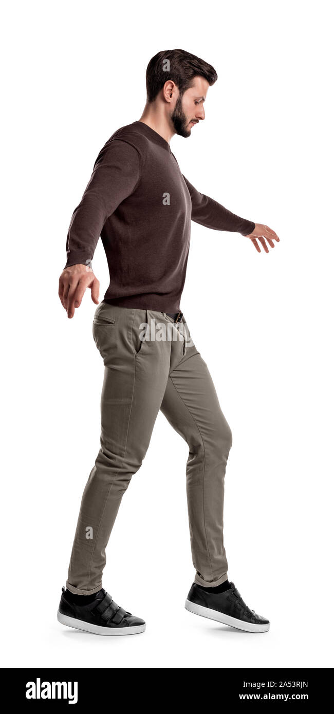 Mettre en place un homme dans des vêtements décontractés regarde comme il lève son pied pendant les étapes de marche funambule sur un fond blanc. Banque D'Images