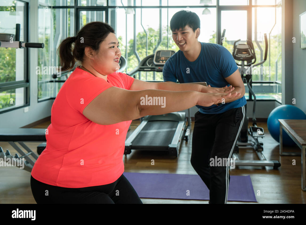 Deux formateurs de l'Asie et de l'embonpoint homme femme stretch exercice ensemble dans une salle de sport moderne, heureux et sourire pendant l'entraînement. Grosses femmes prendre soin de la santé un Banque D'Images