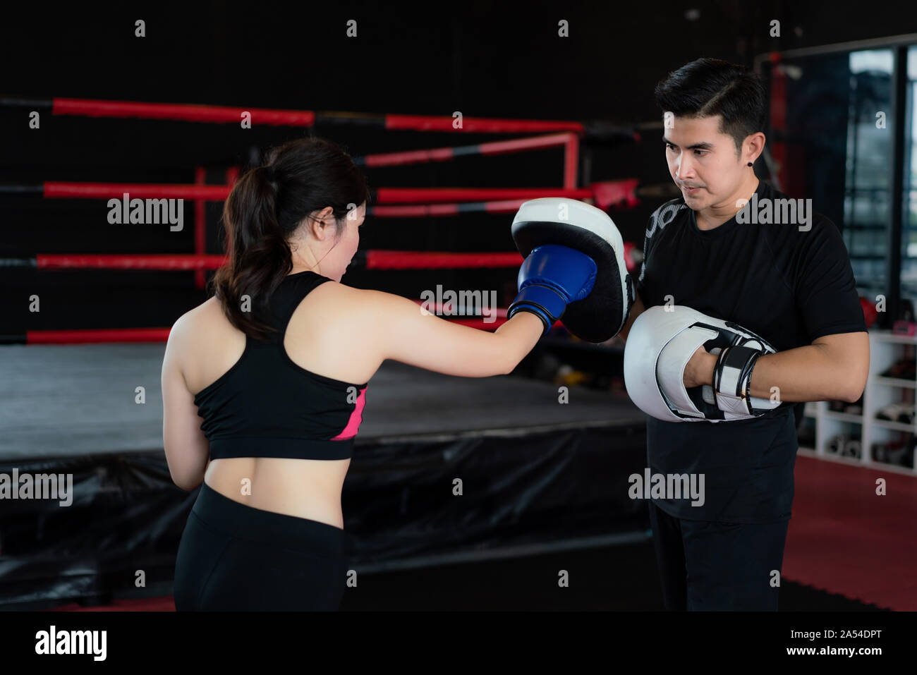 Young Asian woman boxer frappe avec poinçon Droit à formateur professionnel dans la boxe à l'arrière-plan studuim au fitness. Mettre en place pour une sportive Banque D'Images