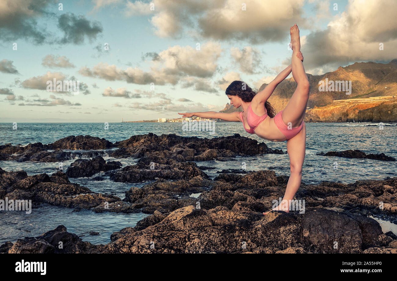 Woman practicing yoga in formation de roche volcanique. Nuages de fond Banque D'Images