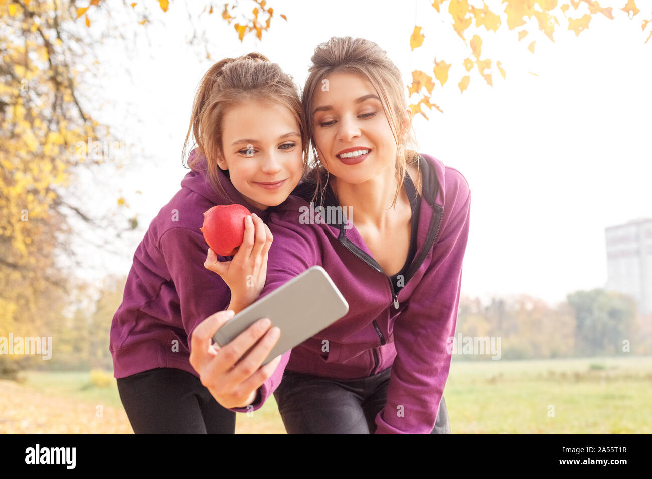 Loisirs de plein air. Soeurs article hugging in l'automne park en tenant sur smartphone selfies avec apple smiling smiling Banque D'Images