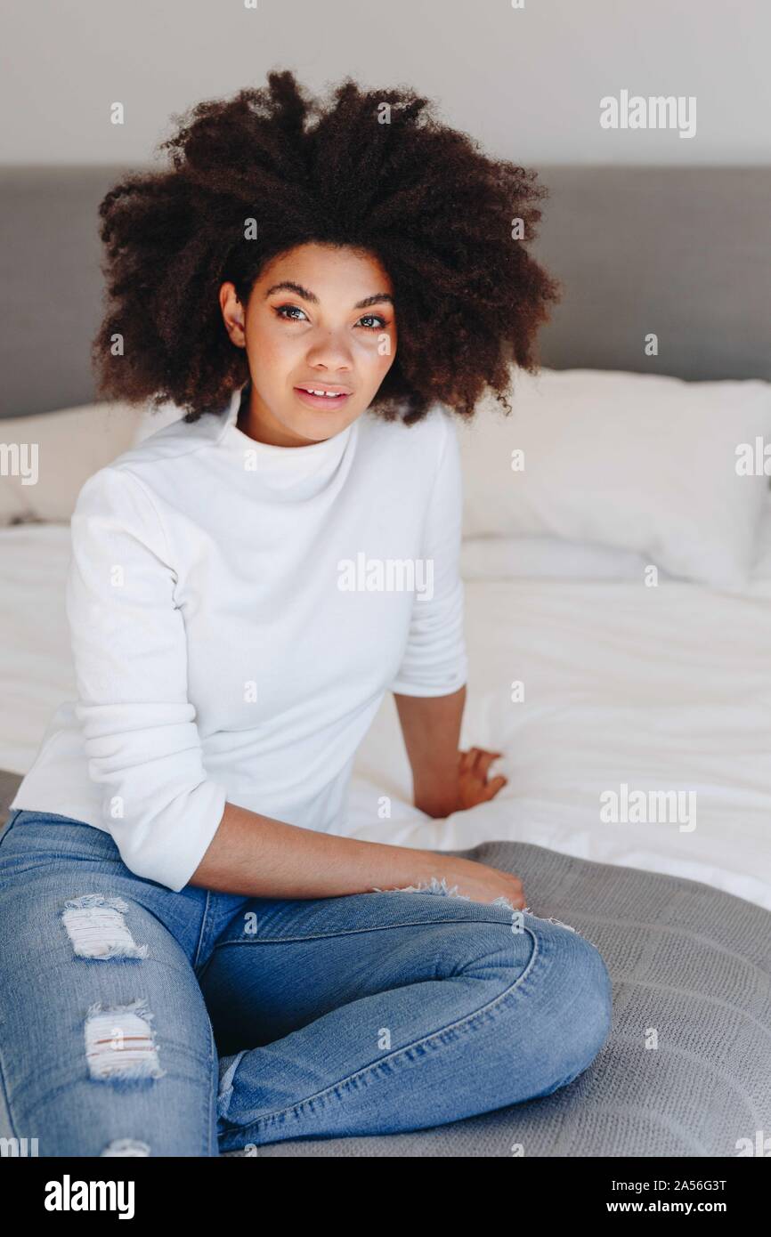 Jeune femme avec coiffure afro sitting on bed, portrait Banque D'Images