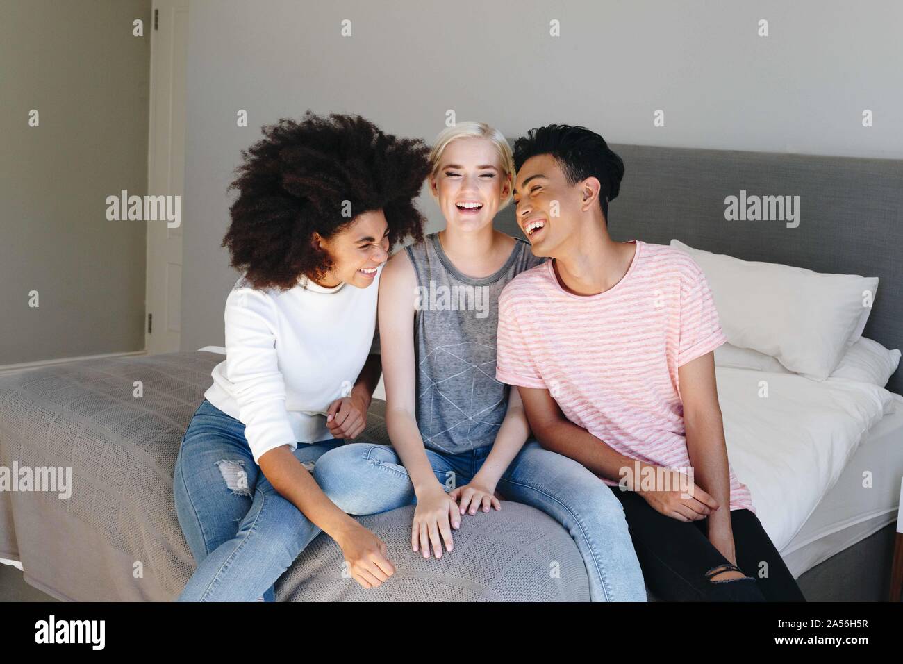 Jeune homme et deux femmes friends sitting on bed laughing Banque D'Images